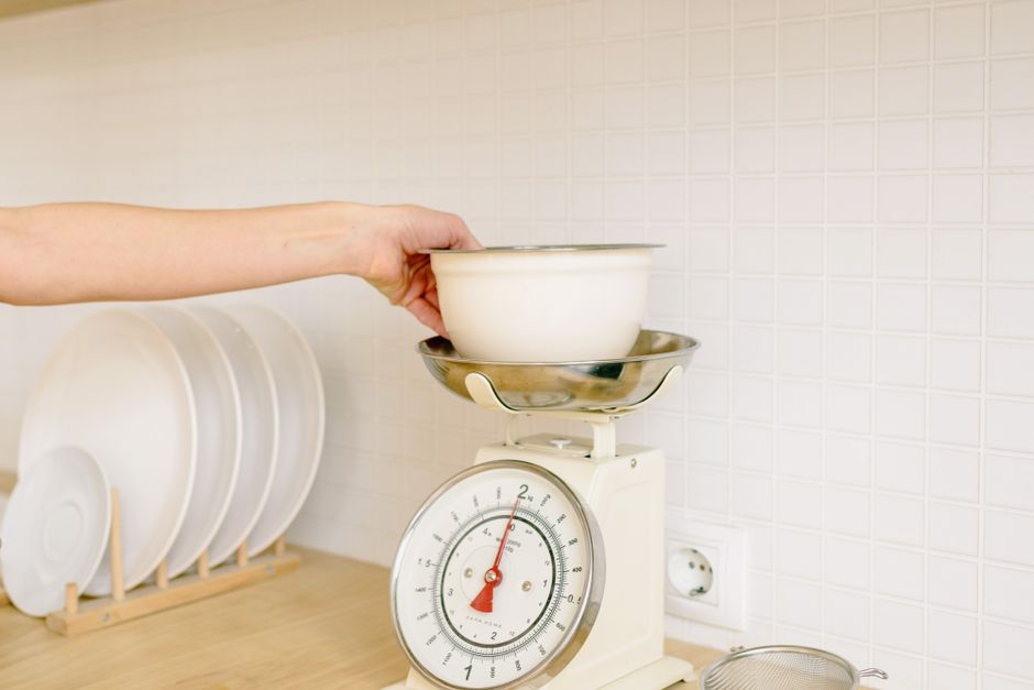 Person weighing ingredients on kitchen scales while tracking food