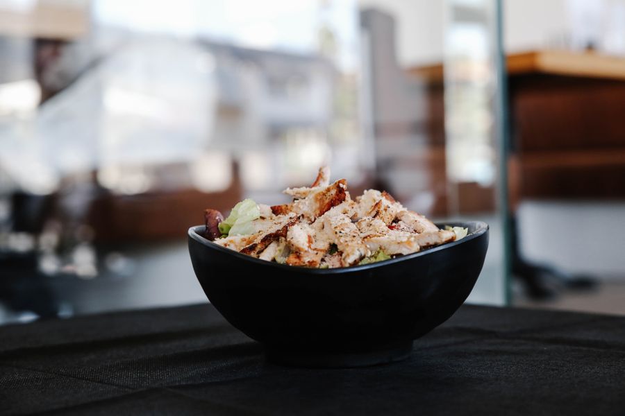 A black bowl of sliced grilled chicken over salad leaves on a table