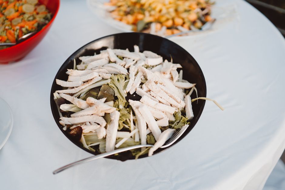 A bowl of sliced grilled chicken over salad leaves and vegetables, served on a table