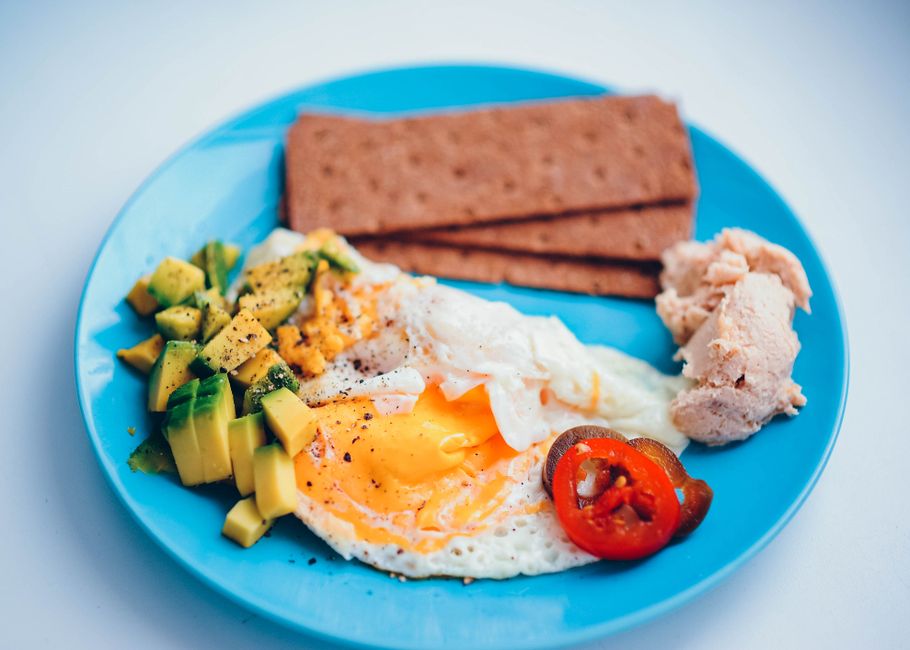 A breakfast plate with a fried egg, diced avocado, rye crispbread, salmon pate and sliced chilli