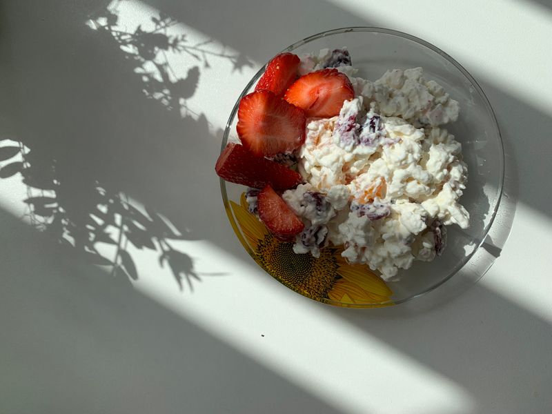 A glass bowl of cottage cheese with sliced strawberries, lit by morning sun