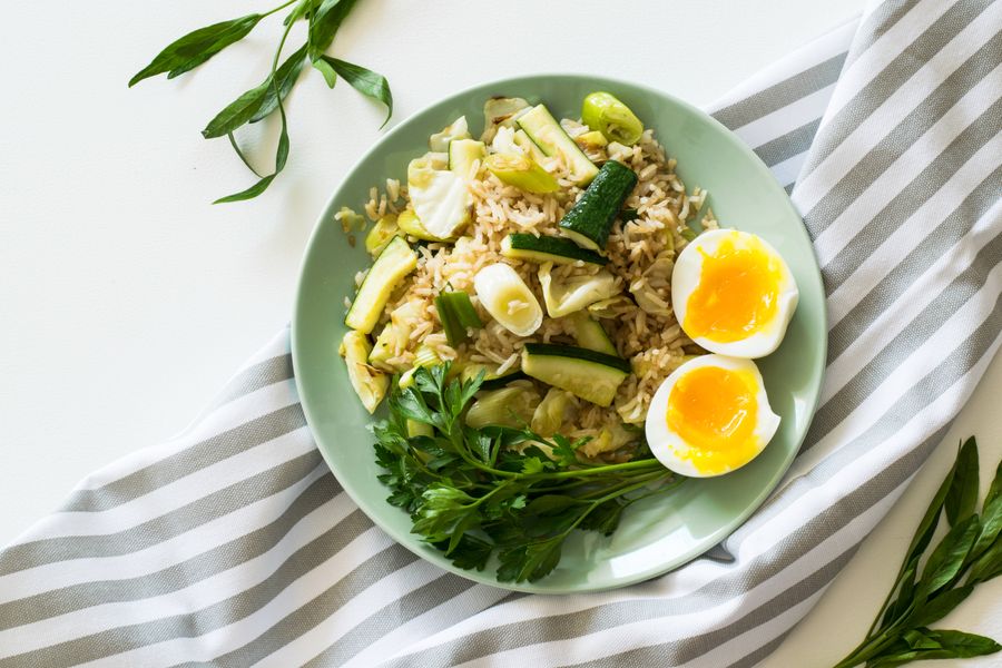 A plate of rice with courgette and spring onion, served with two halves of a soft-boiled egg and fresh parsley